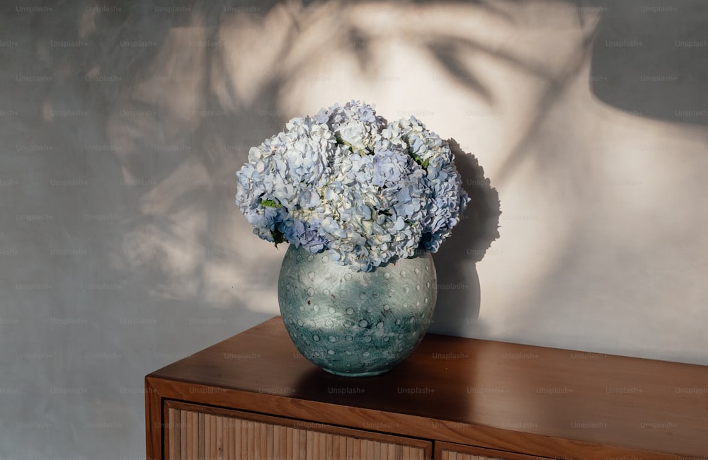 eine Vase mit Blumen, die auf einem Holzschrank sitzt