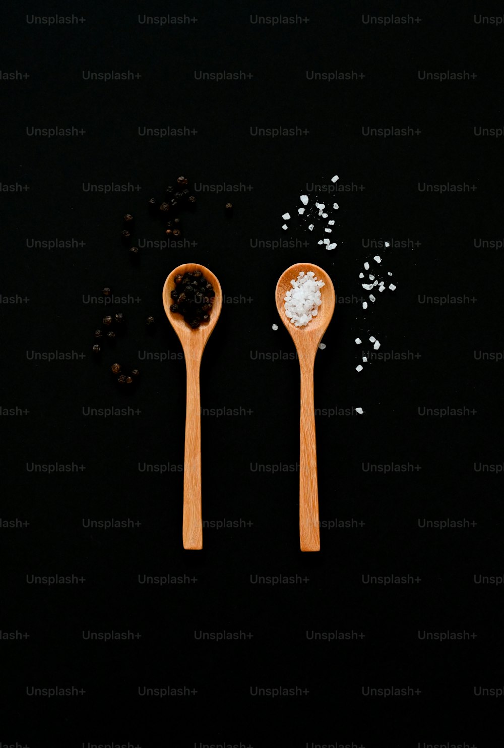 two wooden spoons with salt and pepper on a black surface