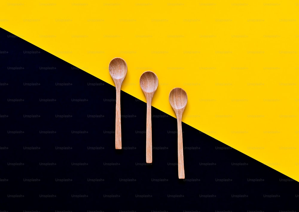 three wooden spoons sitting next to each other on a yellow and black background