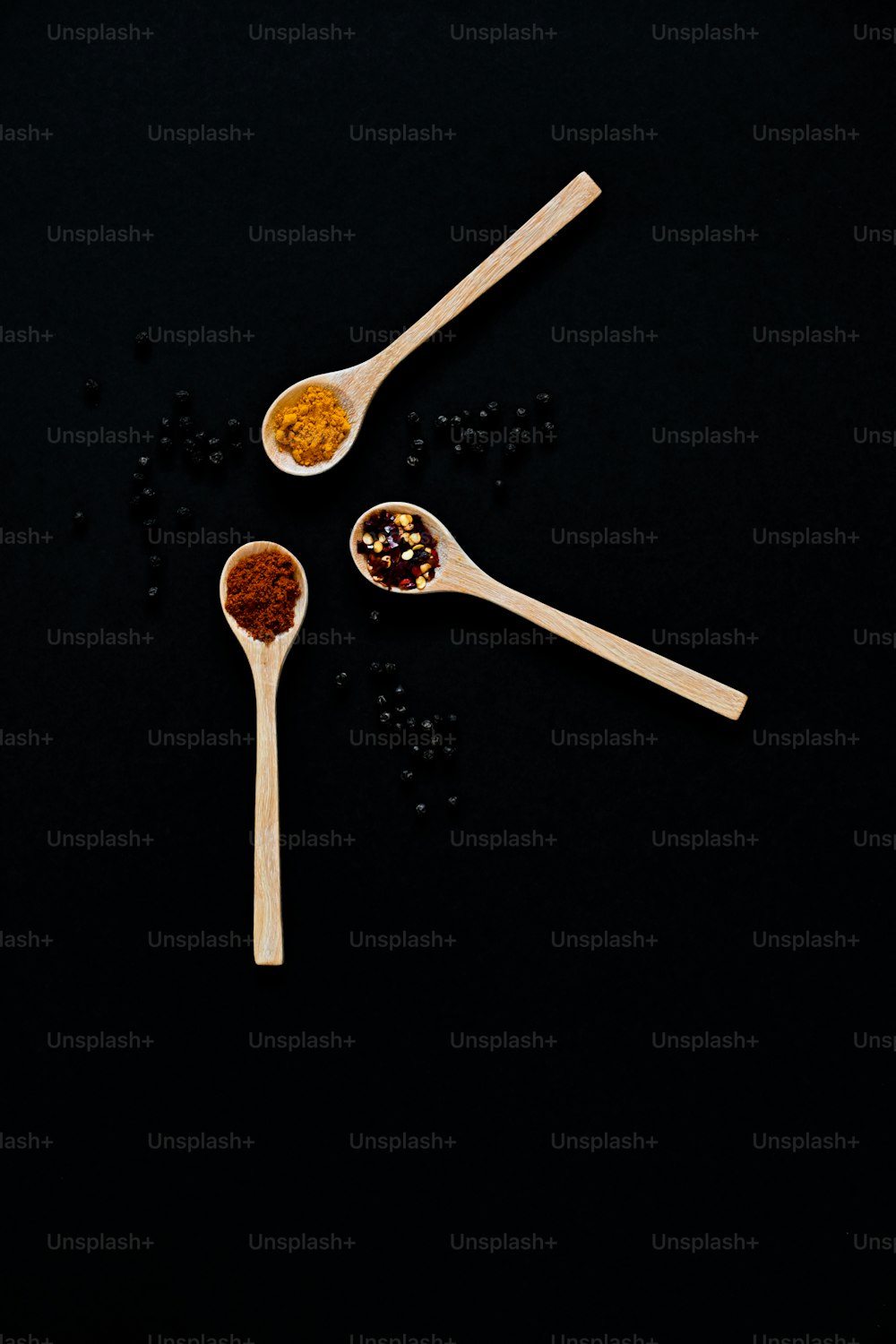 three wooden spoons filled with spices on a black surface