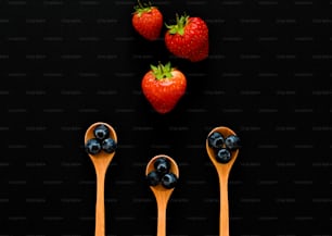 three wooden spoons with blueberries and strawberries on them