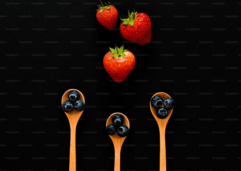 three wooden spoons with blueberries and strawberries on them