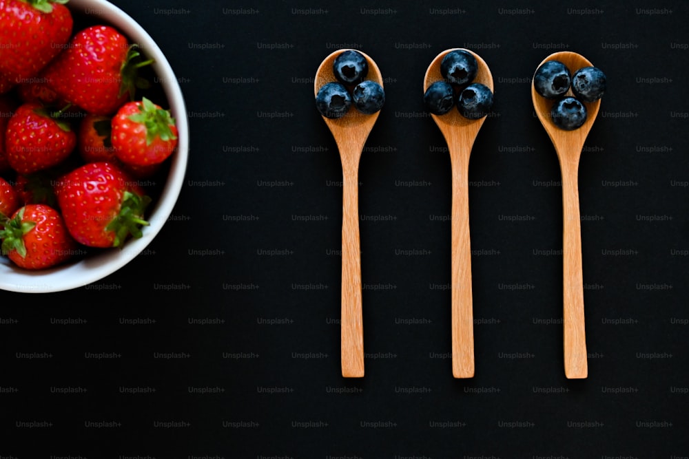 three wooden spoons with blueberries and strawberries in them