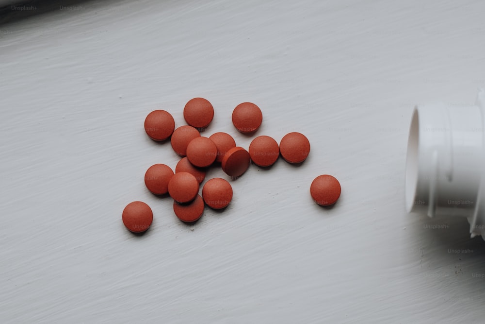 Un contenitore bianco pieno di pillole rosse in cima a un tavolo