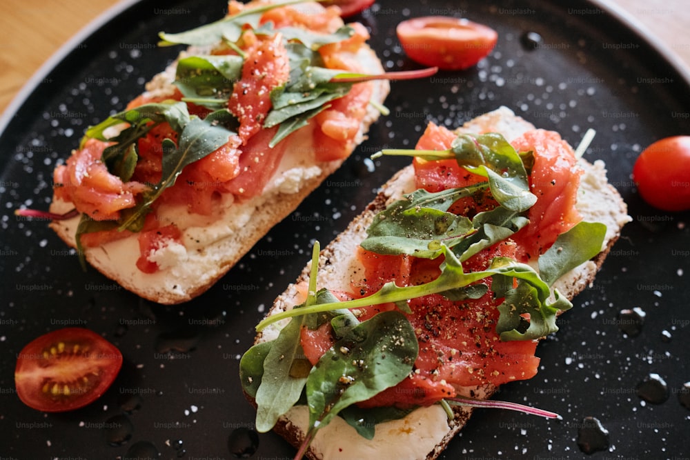 a black plate topped with two pieces of bread covered in toppings