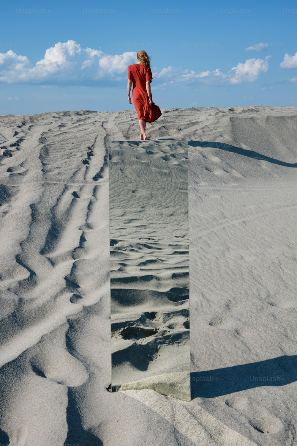 빨간 드레스를 입은 여자가 모래 위를 걷고 있다