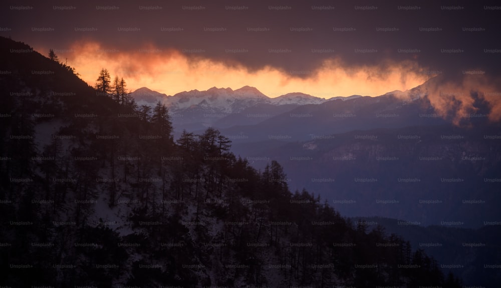 the sun is setting over the mountains and trees