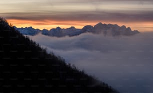 a mountain covered in fog and clouds at sunset