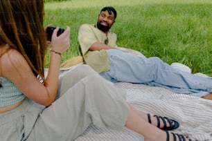 a man and a woman sitting on a blanket in the grass
