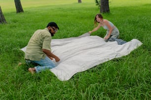 a man and a woman setting up a blanket in the grass