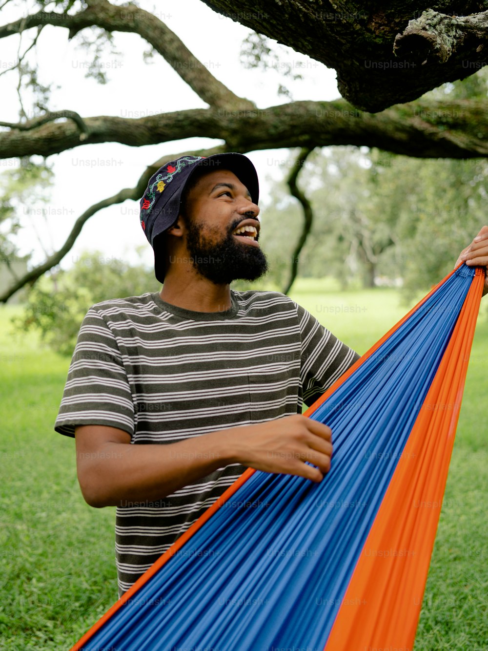a man holding a blue and orange hammock under a tree