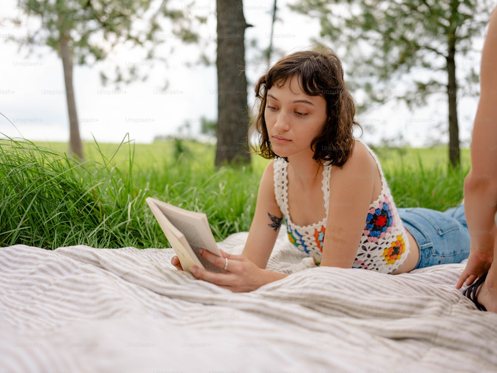 a woman laying on a blanket reading a book
