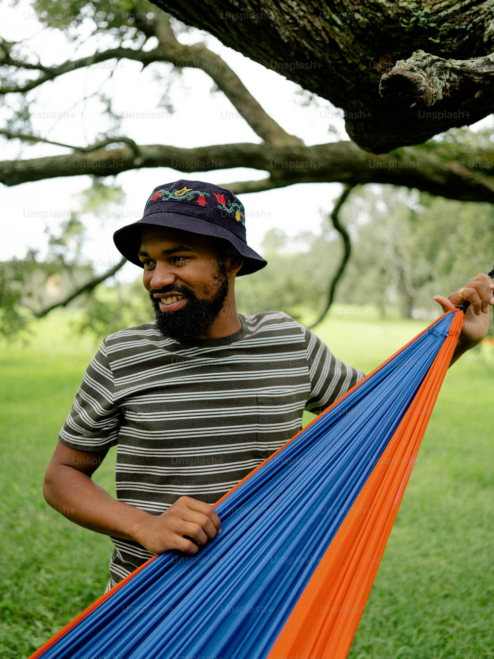 a man holding a blue and orange hammock under a tree