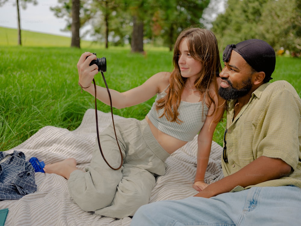 a man and a woman sitting on a blanket with a camera