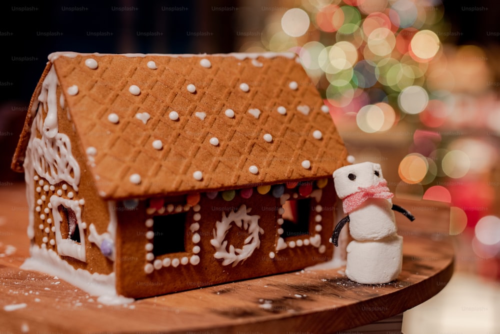 Une maison en pain d’épices avec un bonhomme de neige à côté