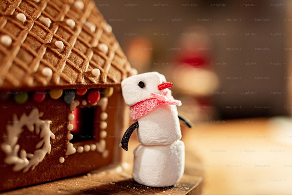 Un primer plano de un muñeco de nieve junto a una casa de pan de jengibre