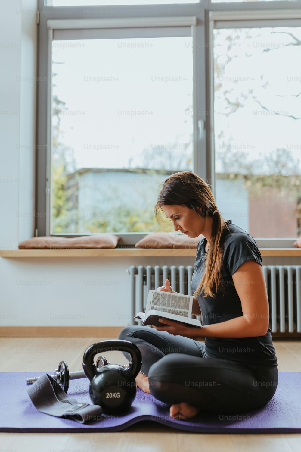 uma pessoa sentada em um tapete de yoga lendo um livro