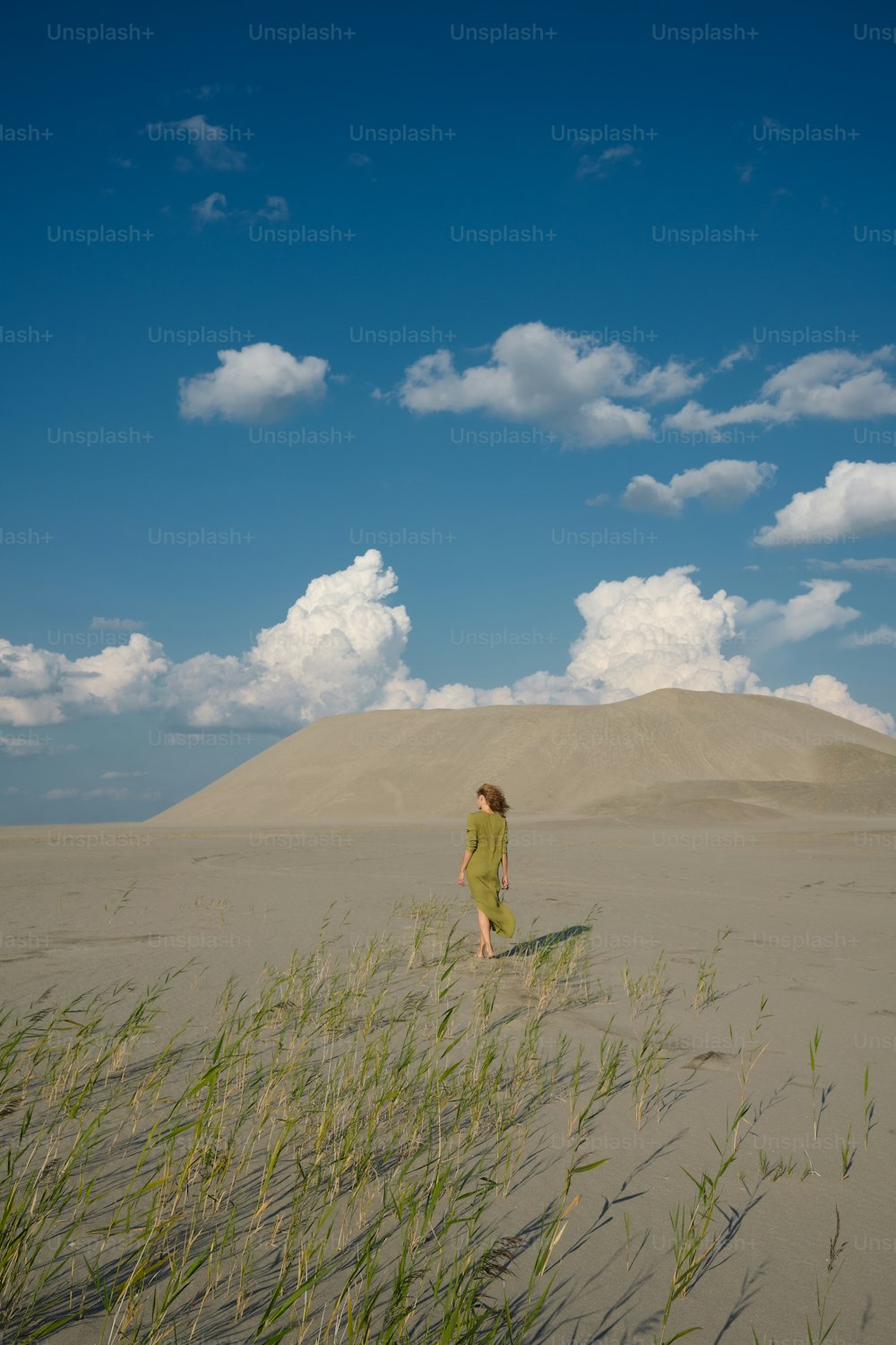 Une femme marchant sur une plage de sable à côté des hautes herbes