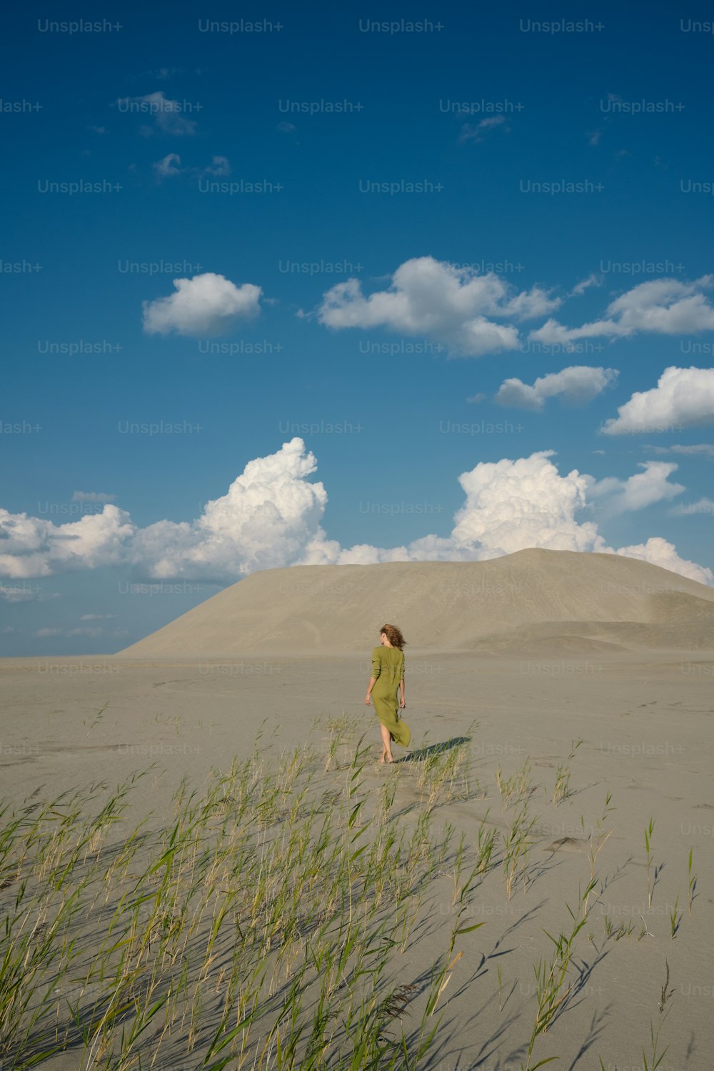 a woman walking across a sandy beach next to tall grass