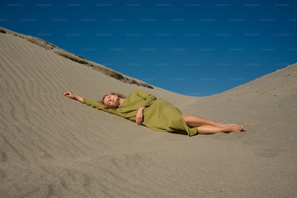 a woman in a green dress laying in the sand