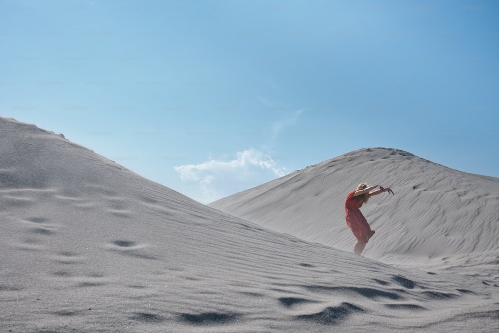 Una mujer con un vestido rojo de pie en la arena