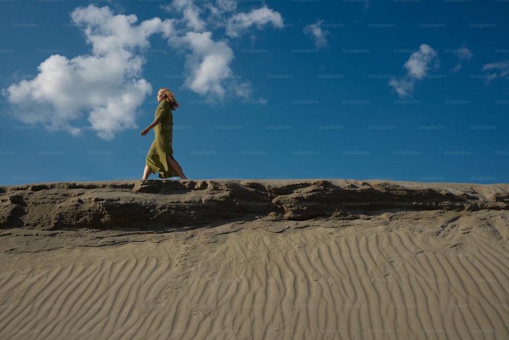 a woman in a green dress is walking on a sand dune
