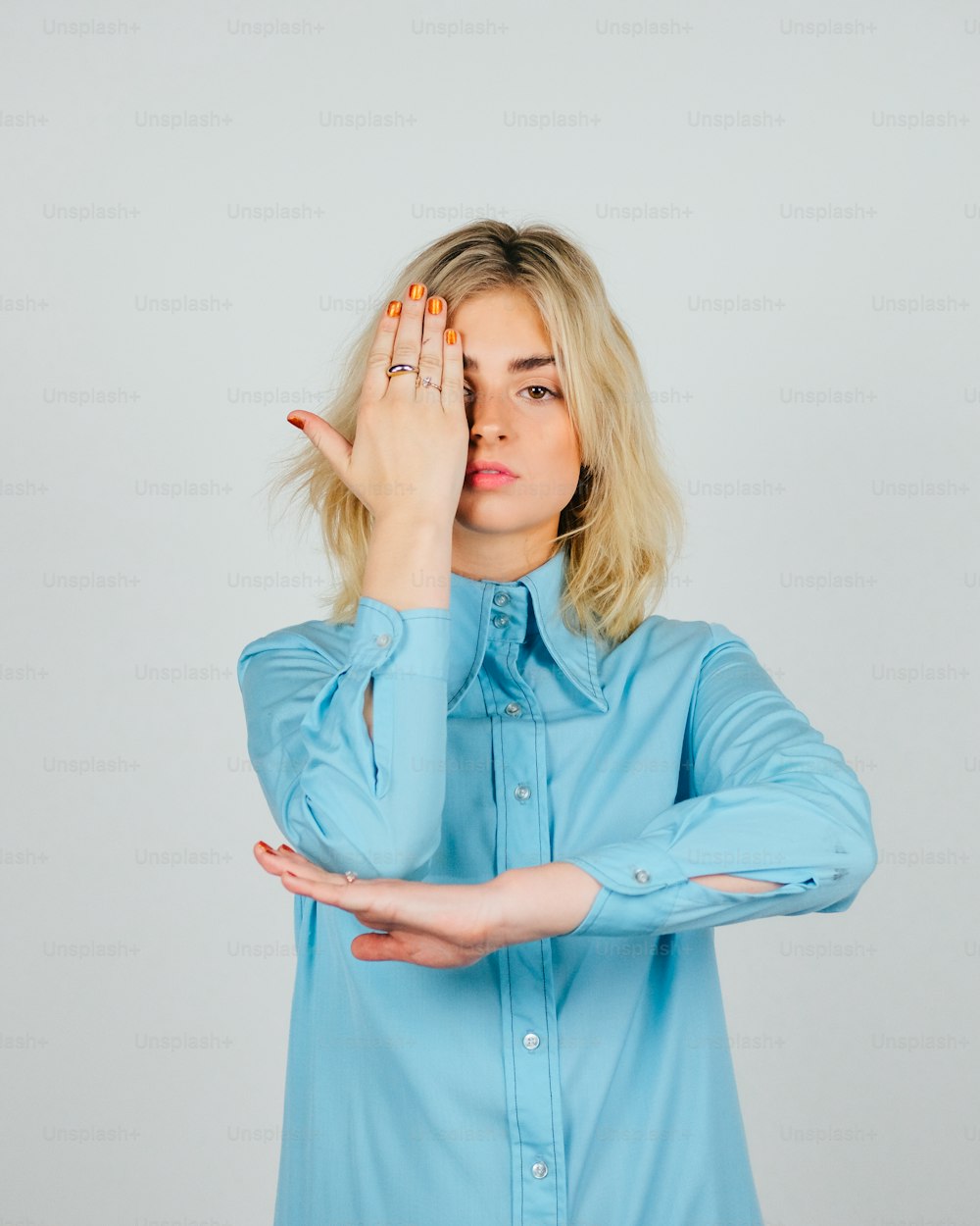 a woman in a blue shirt holding her hands up to her face