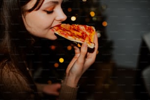 a woman eating a slice of pizza in front of a christmas tree