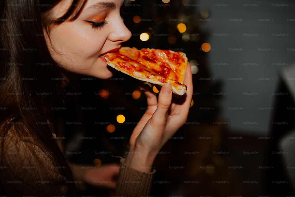 Eine Frau, die ein Stück Pizza vor einem Weihnachtsbaum isst