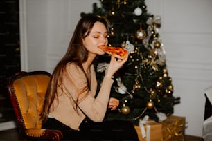 a woman eating a slice of pizza in front of a christmas tree