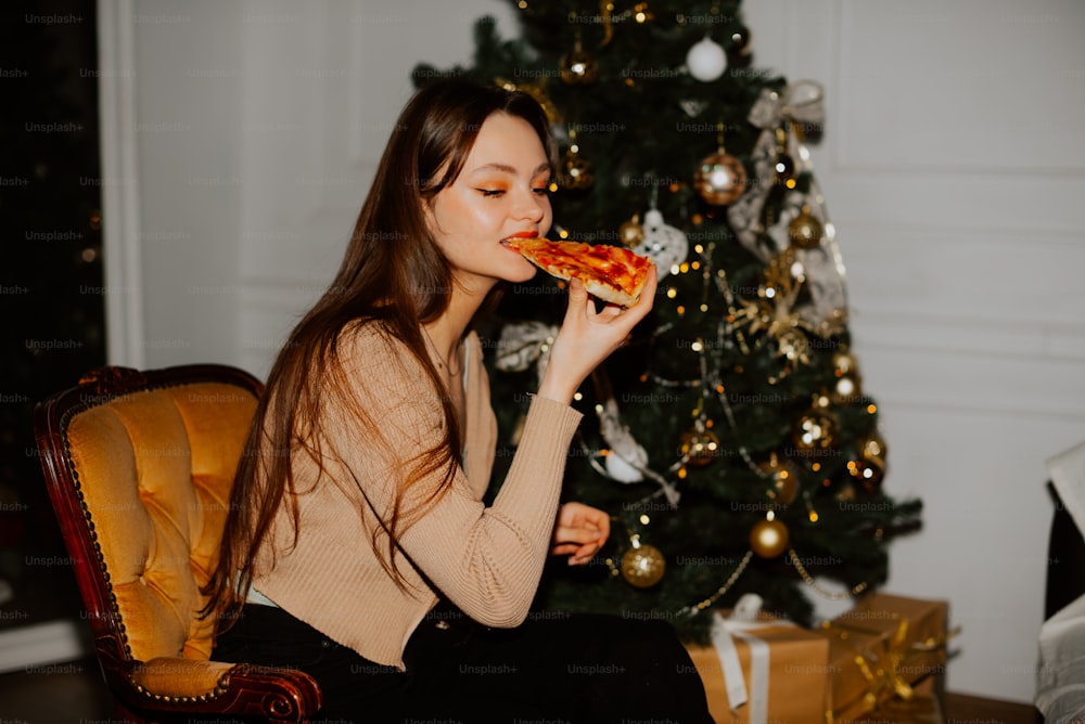 a woman eating a slice of pizza in front of a christmas tree