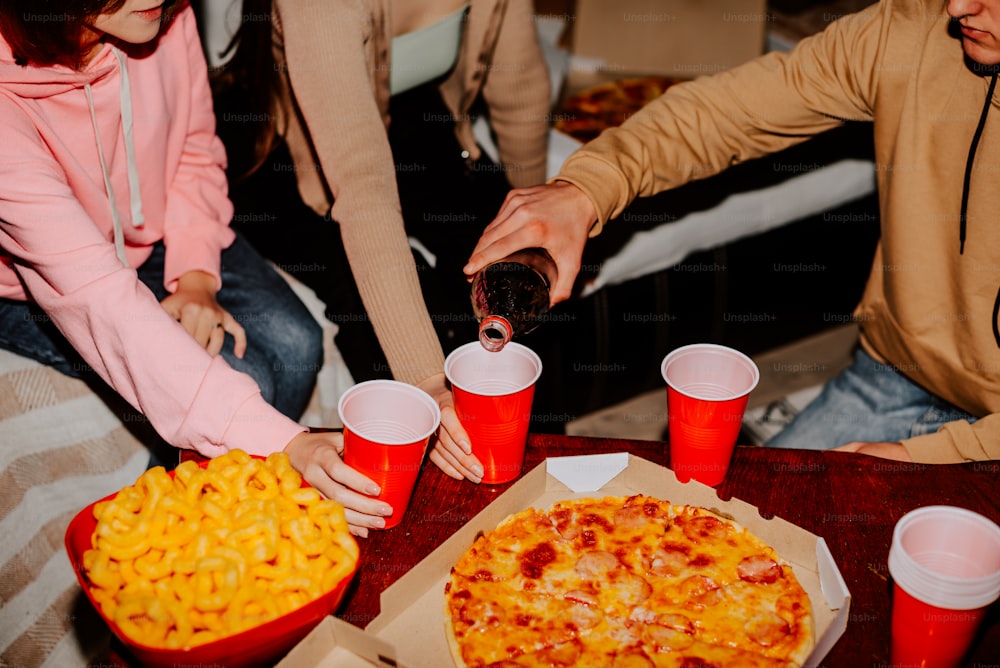 Un grupo de personas sentadas alrededor de una mesa con pizza y bebidas