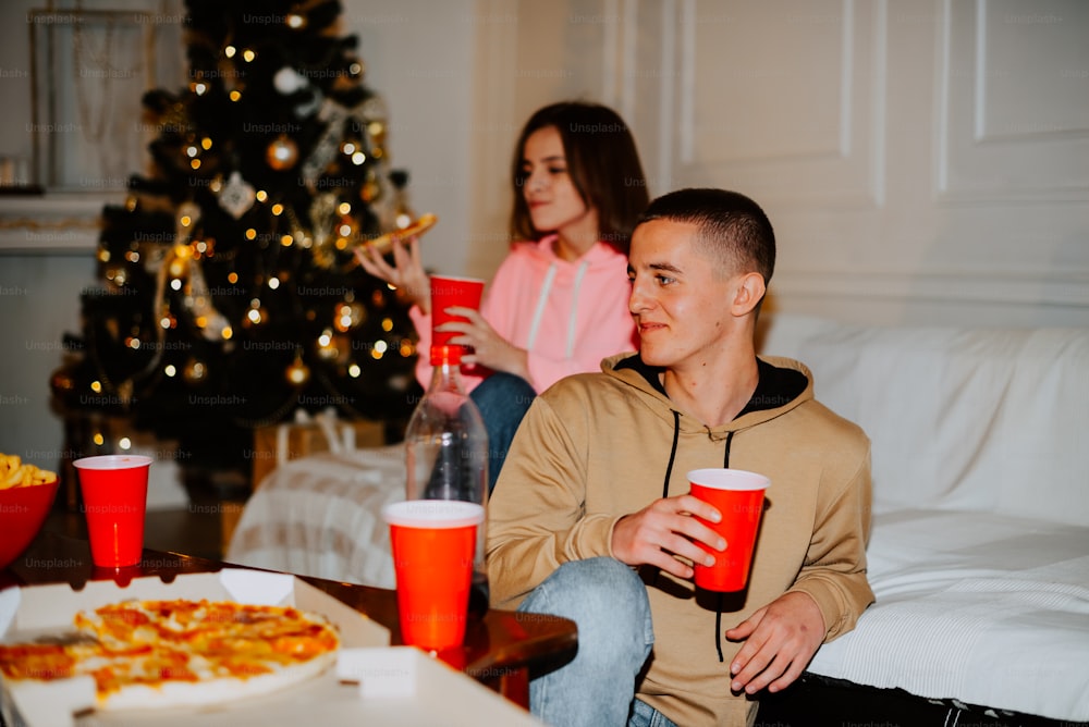 a man and a woman sitting on a couch in front of a christmas tree