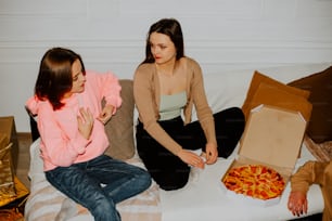 two women sitting on a couch eating pizza
