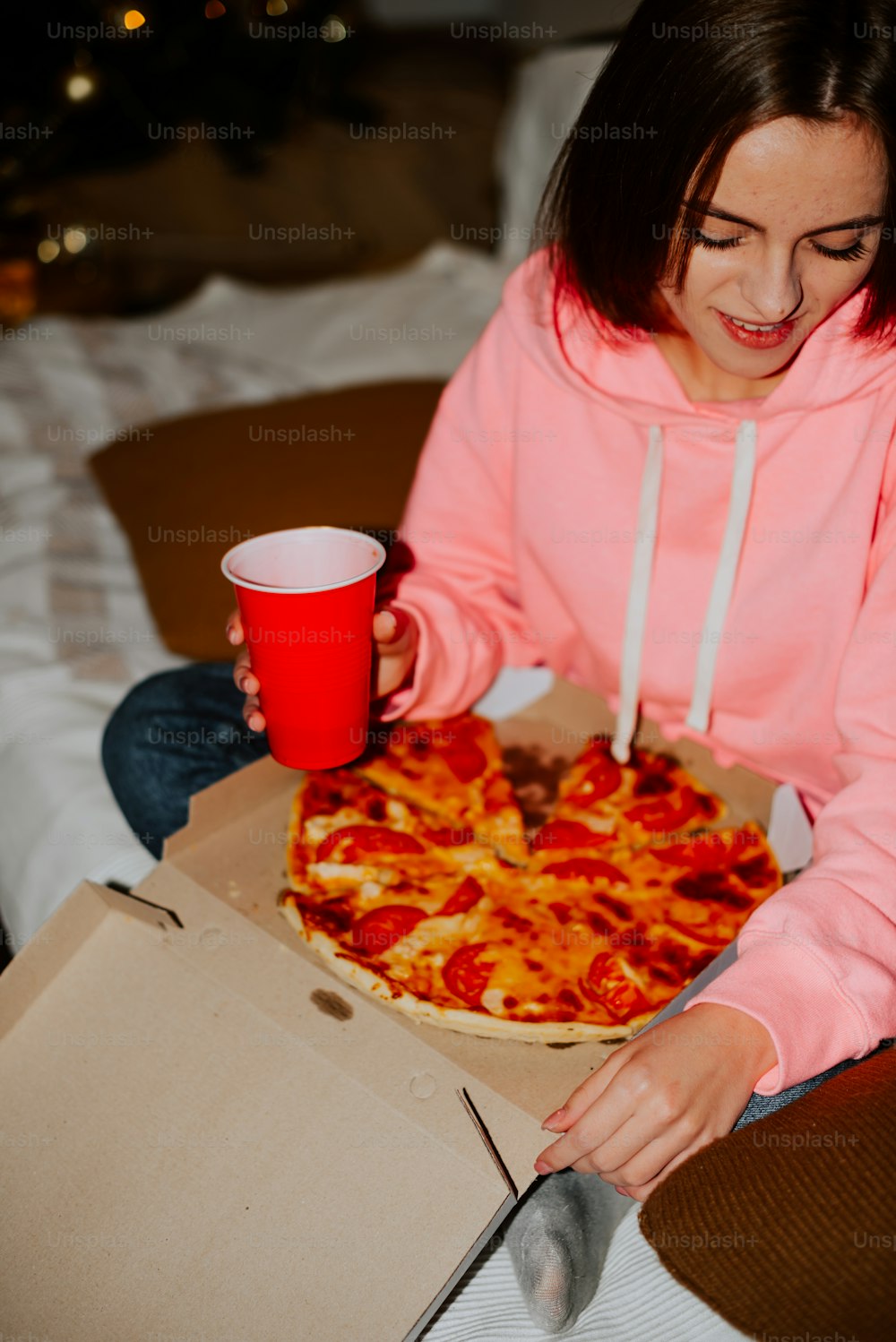 a girl in a pink hoodie holding a red cup and a pizza