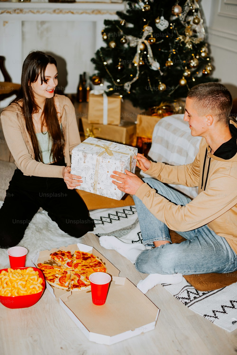 Un hombre y una mujer sentados en el suelo abriendo una caja de pizza
