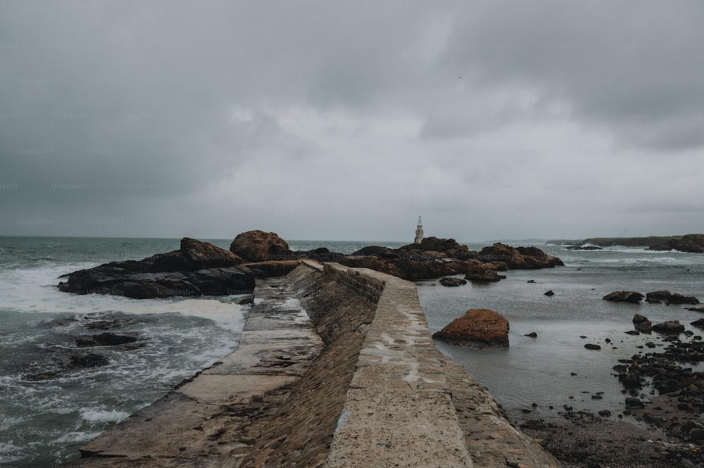 a concrete walkway leading to the ocean under a cloudy sky