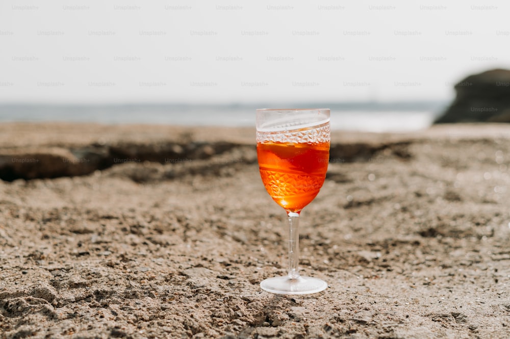 a glass of wine sitting on top of a sandy beach
