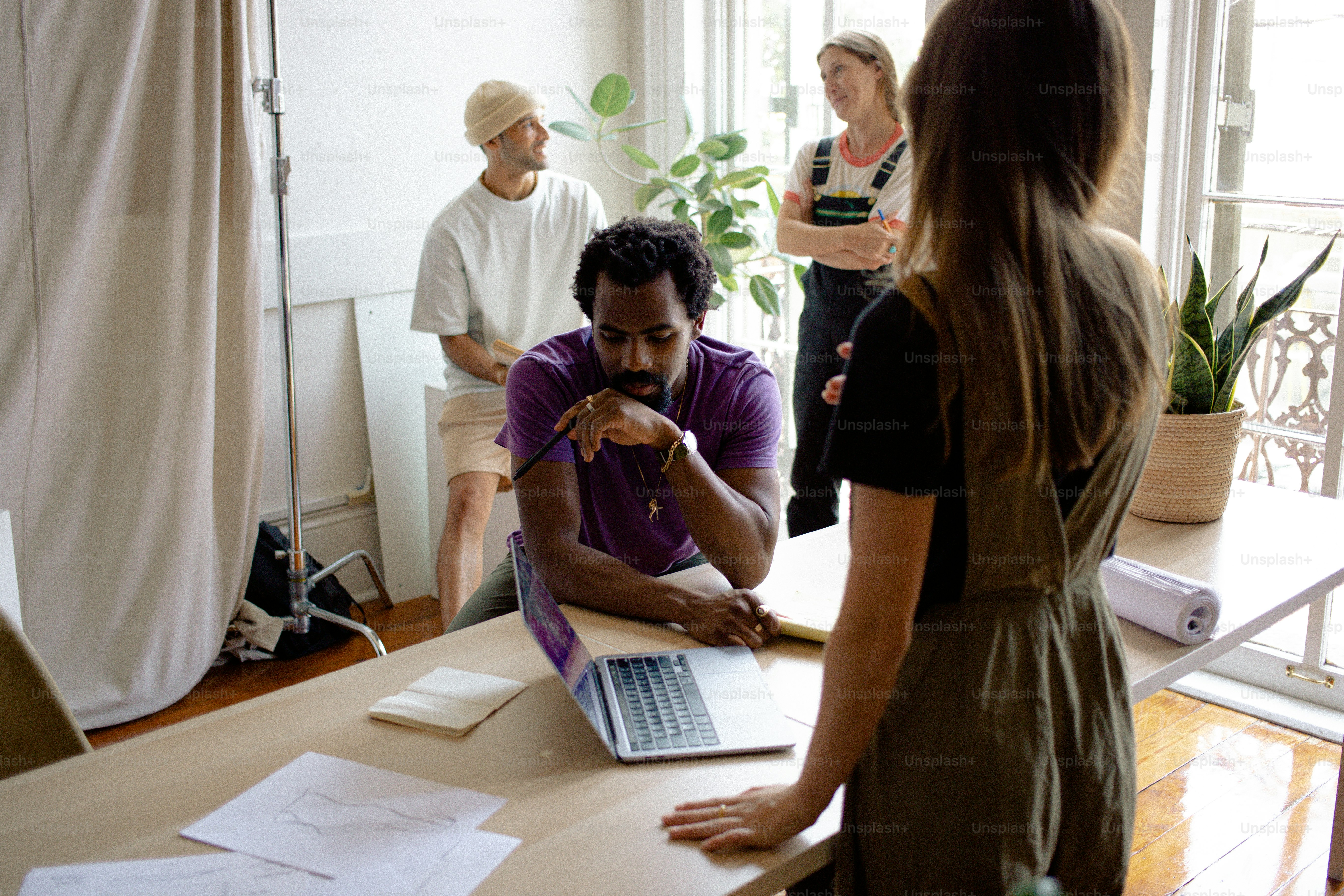A group of people standing around a table with a laptop photo – Working ...
