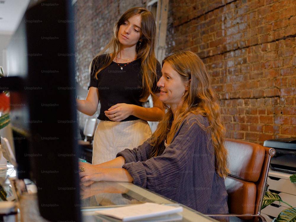 two women sitting at a desk with a computer