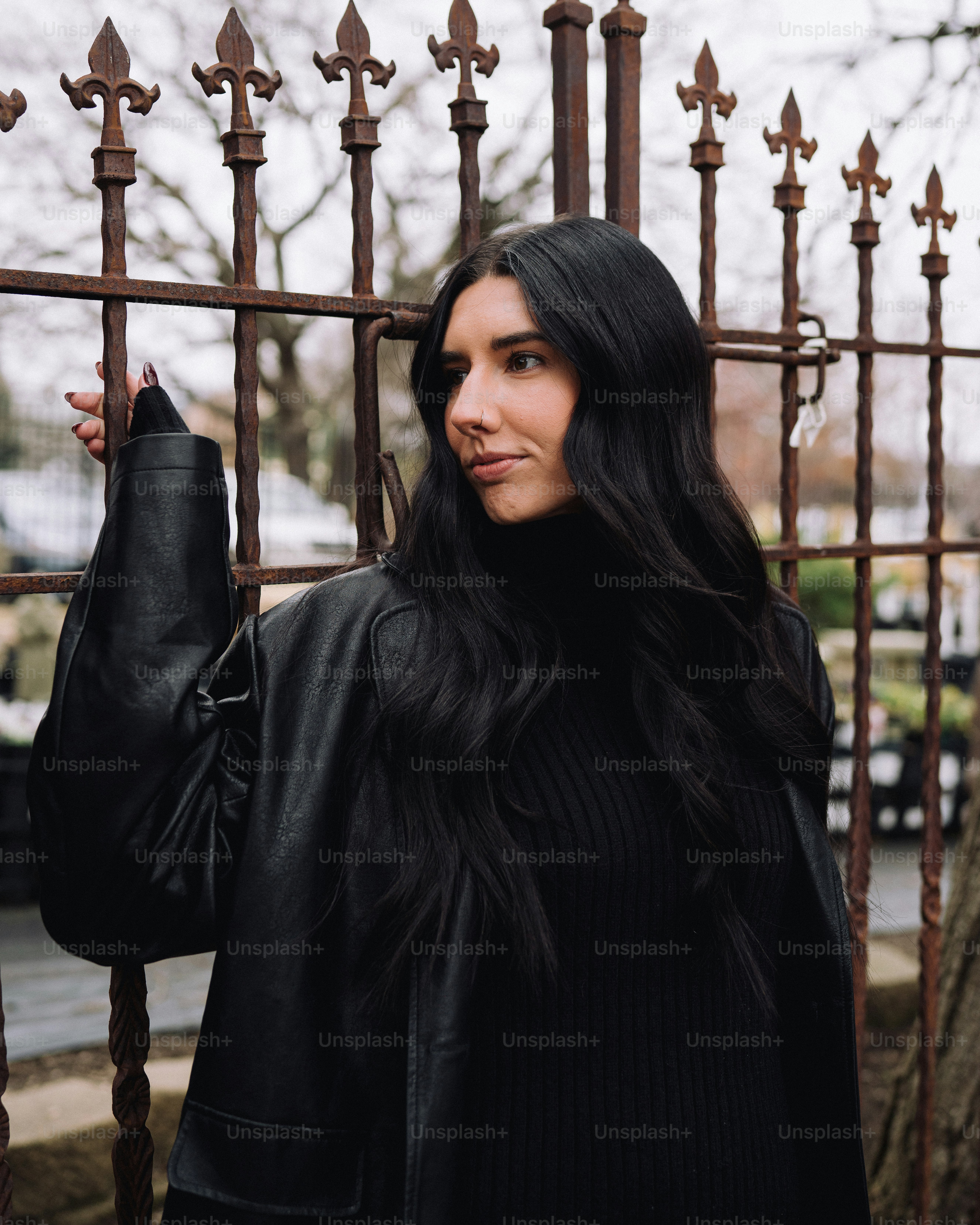 a woman with long black hair standing in front of a fence