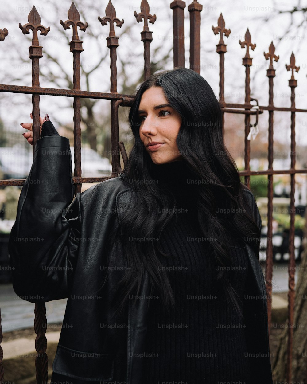 a woman with long black hair standing in front of a fence