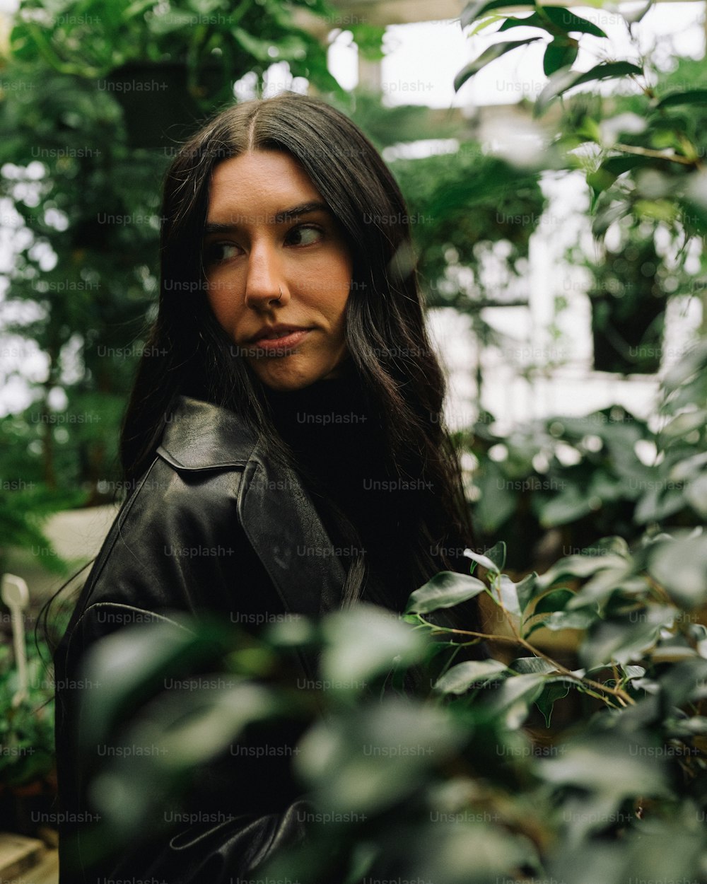 a woman standing in a greenhouse looking at the camera