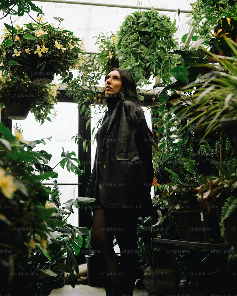 Eine Frau, die in einem Gewächshaus steht, umgeben von Pflanzen;