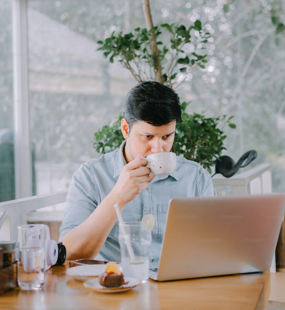 Un uomo seduto a un tavolo con un computer portatile e una tazza di caffè