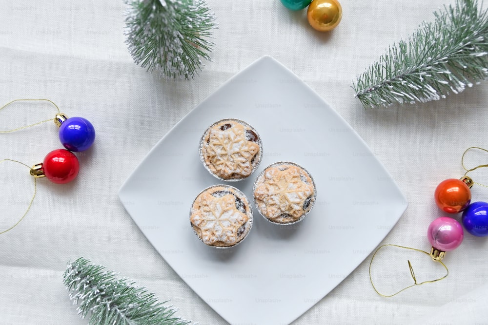 ein weißer Teller mit Muffins neben Weihnachtsschmuck
