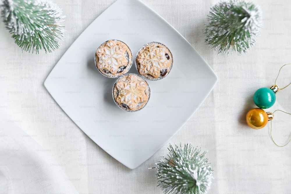 ein weißer Teller mit drei Muffins neben einem Weihnachtsschmuck