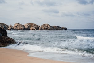 a rocky outcropping in the ocean next to a sandy beach