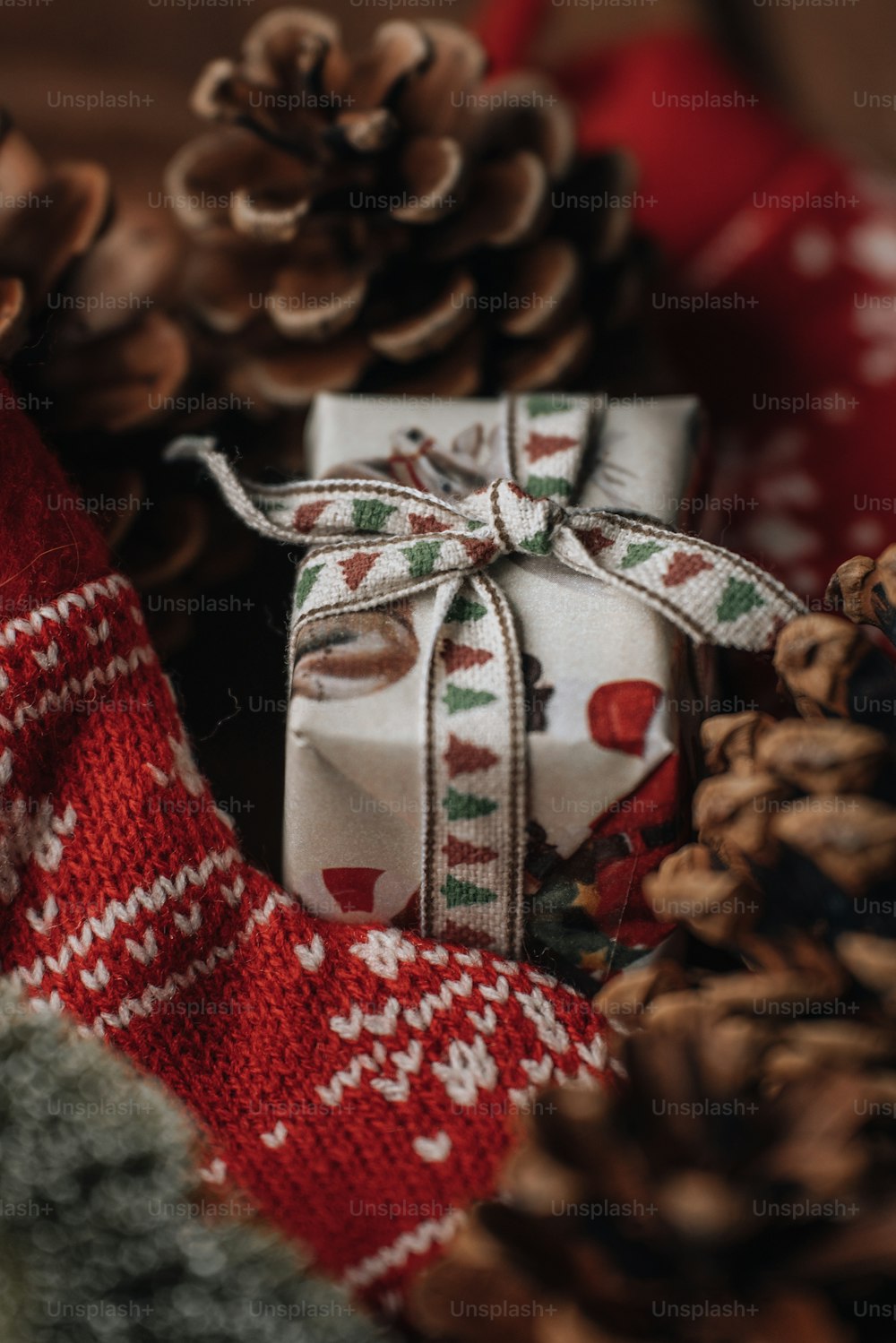 a gift wrapped in a red and white ribbon next to pine cones