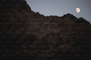 the moon is setting over a rocky mountain